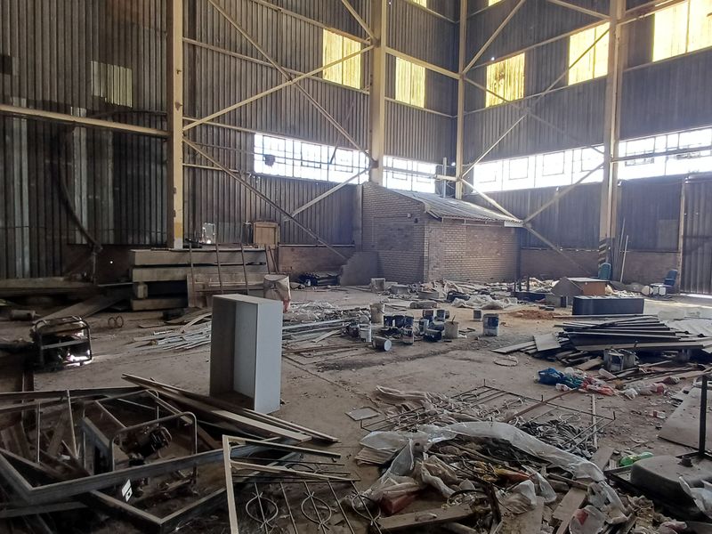 Large industrial warehouse space featuring high ceilings, steel portal frame construction, and concrete flooring, currently requiring significant clearing and refurbishment.