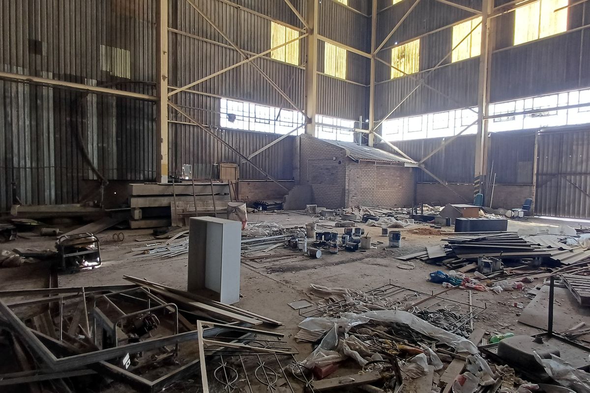 Large industrial warehouse space featuring high ceilings, steel portal frame construction, and concrete flooring, currently requiring significant clearing and refurbishment.
