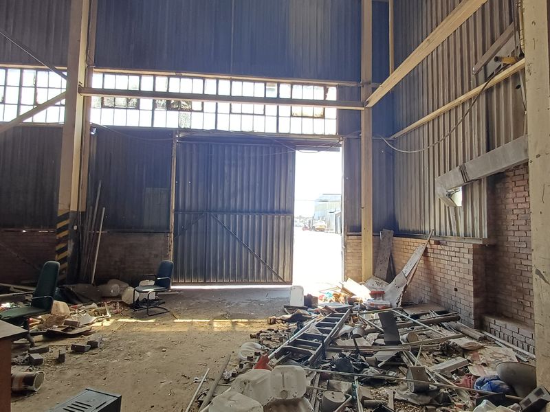 Spacious industrial utility area featuring high ceilings, exposed brickwork, steel structural columns, and large sliding access doors, currently requiring significant clearing and refurbishment.