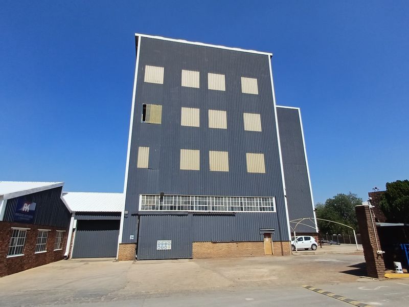 Front elevation of a multi-story industrial facility featuring corrugated metal cladding, brickwork, and large industrial sliding doors.