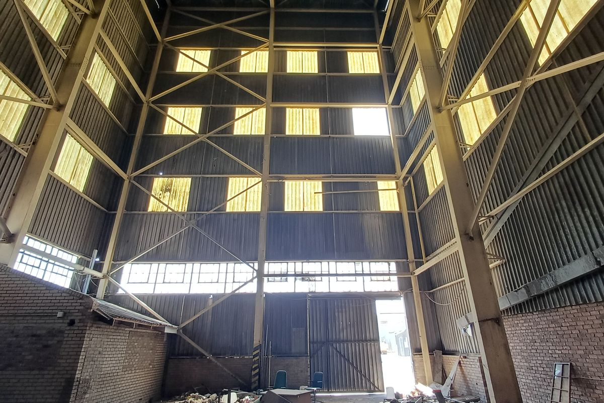 Expansive industrial utility space featuring a high-clearance steel portal frame, corrugated metal walls, and translucent panels providing natural overhead lighting.