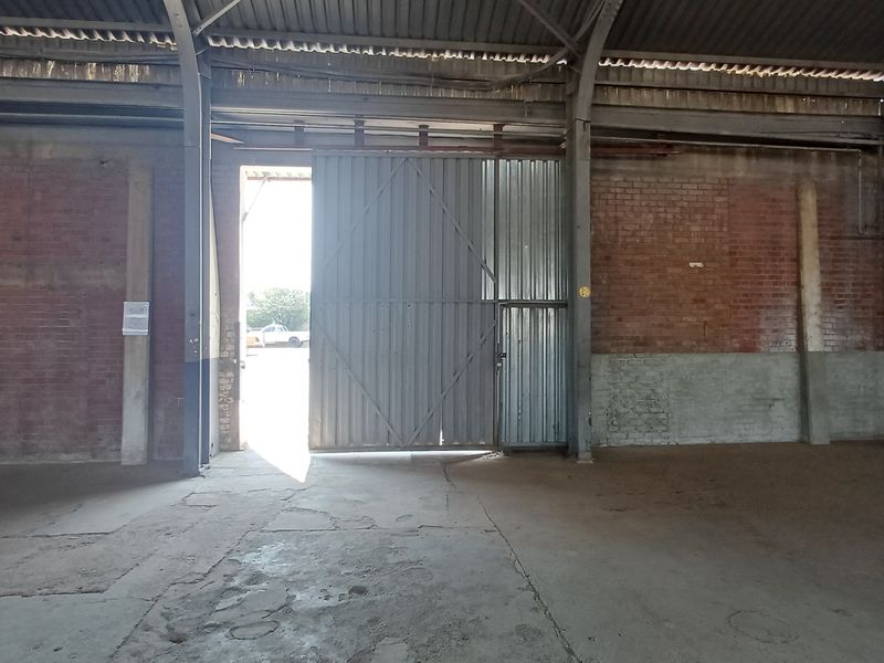 Spacious industrial utility area featuring exposed brick walls, concrete flooring, and a large sliding metal access door within a steel portal frame structure.