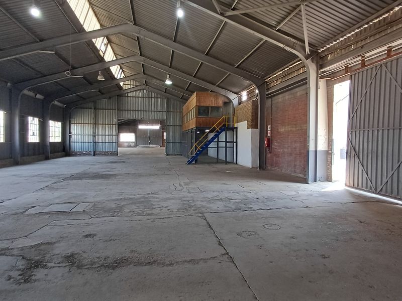 Spacious industrial warehouse featuring high ceilings, concrete flooring, large sliding access doors, and an integrated mezzanine office structure.