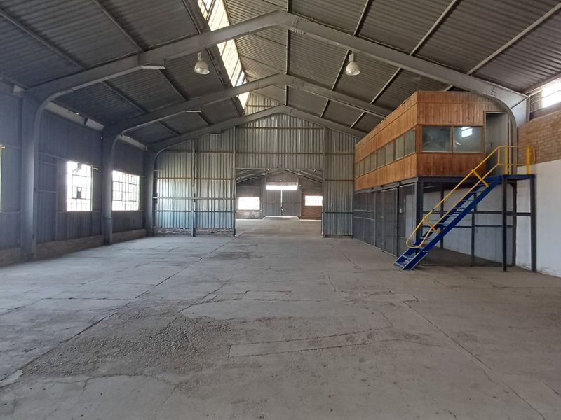 Spacious industrial warehouse featuring a high-clearance steel portal frame, concrete flooring, and an integrated mezzanine office level with staircase access.