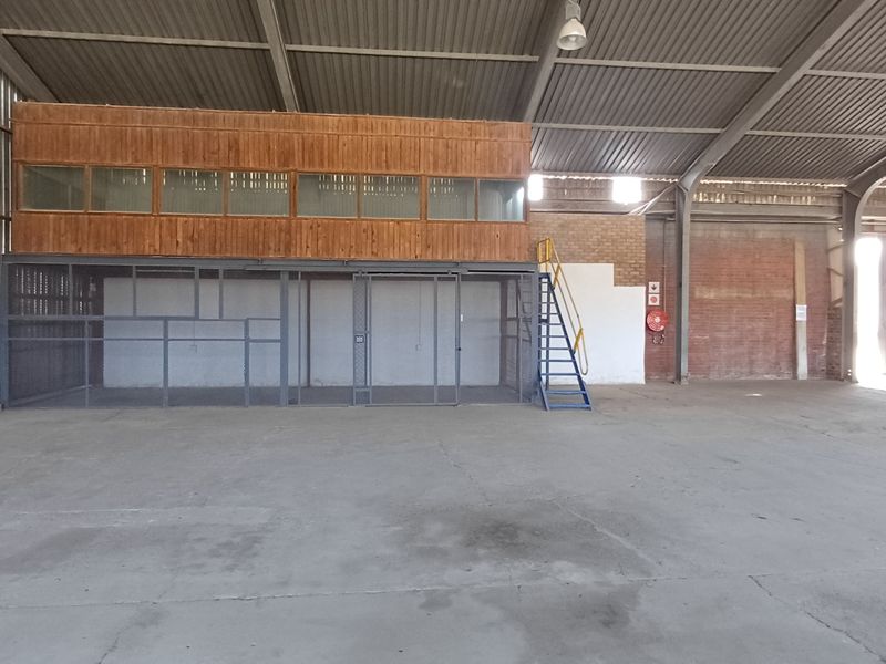 Spacious industrial warehouse featuring a concrete floor, high-clearance corrugated roof, and a built-in mezzanine office structure with an integrated security cage.