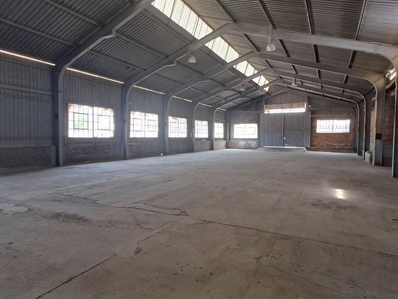 Spacious industrial warehouse featuring a steel portal frame, concrete flooring, natural skylight illumination, and large sliding access doors.