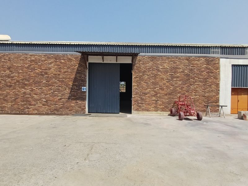 Industrial warehouse exterior featuring a brick facade, corrugated metal roofing, and a large sliding entrance door with a concrete apron.
