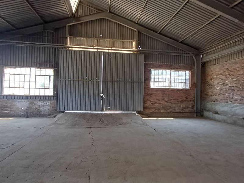 Spacious industrial warehouse featuring a high-clearance steel portal frame, concrete flooring, brick walls, and large sliding access doors.