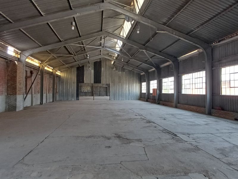 Spacious industrial warehouse featuring a high-clearance steel portal frame, concrete flooring, and large steel-framed windows providing ample natural light.