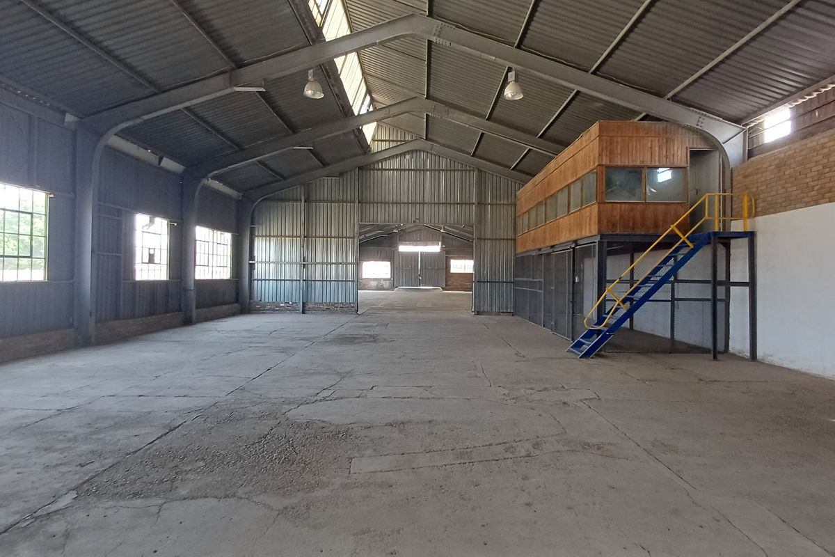 Spacious industrial warehouse featuring a high-clearance steel portal frame, concrete flooring, and an integrated mezzanine office level with staircase access.