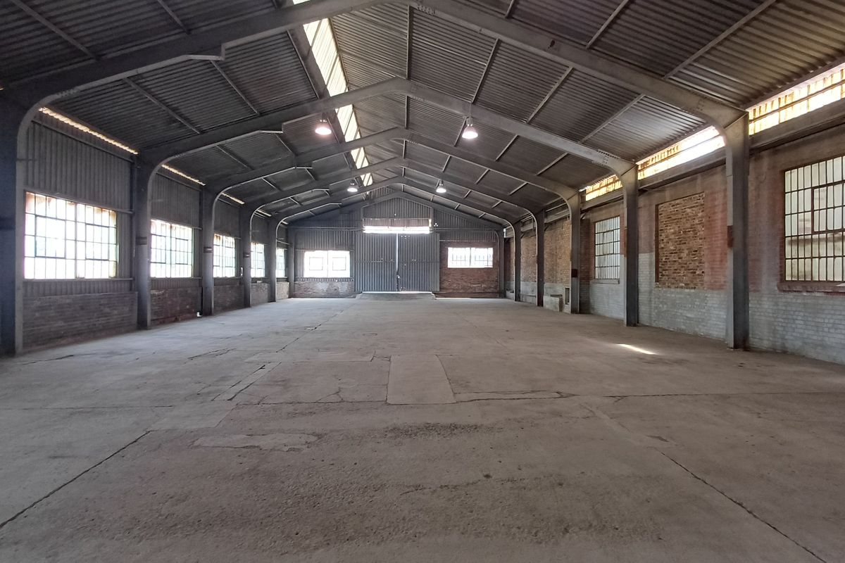 Spacious industrial warehouse featuring a high-clearance steel portal frame, concrete flooring, exposed brick walls, and large steel-framed windows providing ample natural light.