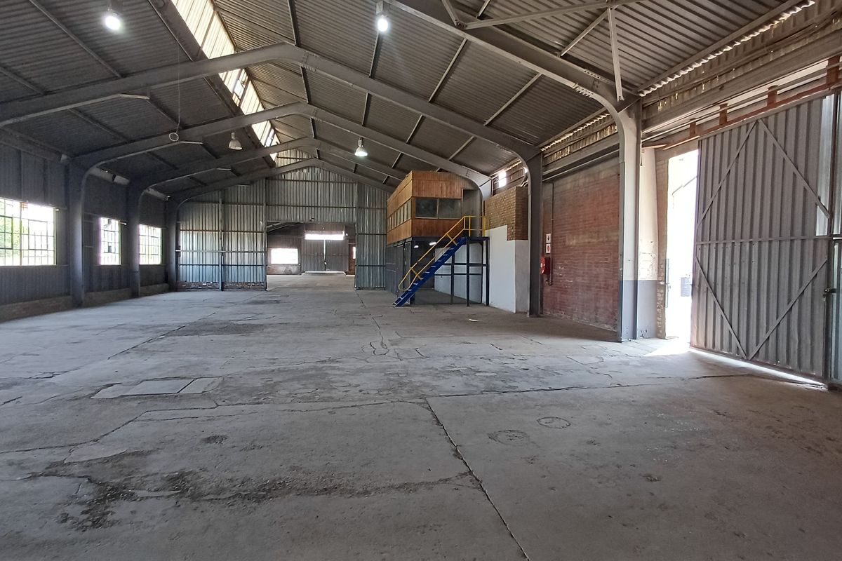 Spacious industrial warehouse featuring high ceilings, concrete flooring, large sliding access doors, and an integrated mezzanine office structure.