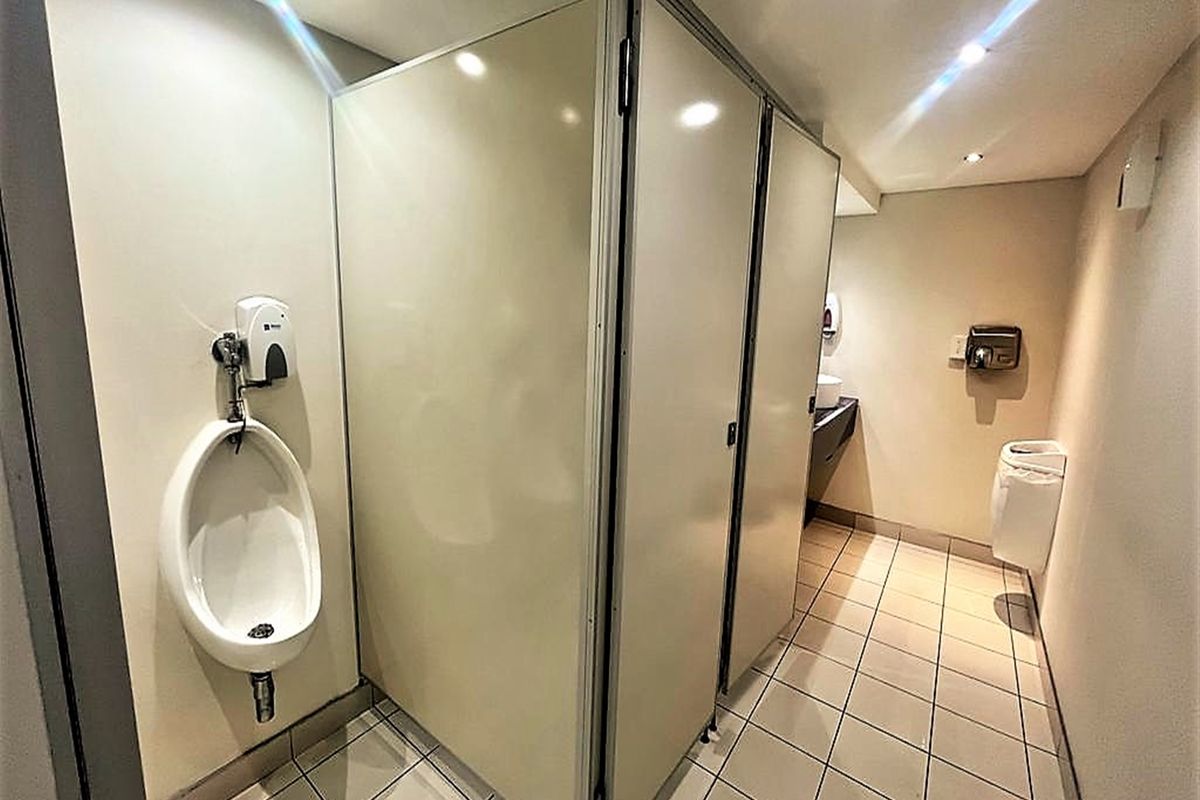A functional office restroom featuring tiled flooring, multiple toilet cubicles, and wall-mounted sanitary fixtures including a urinal.