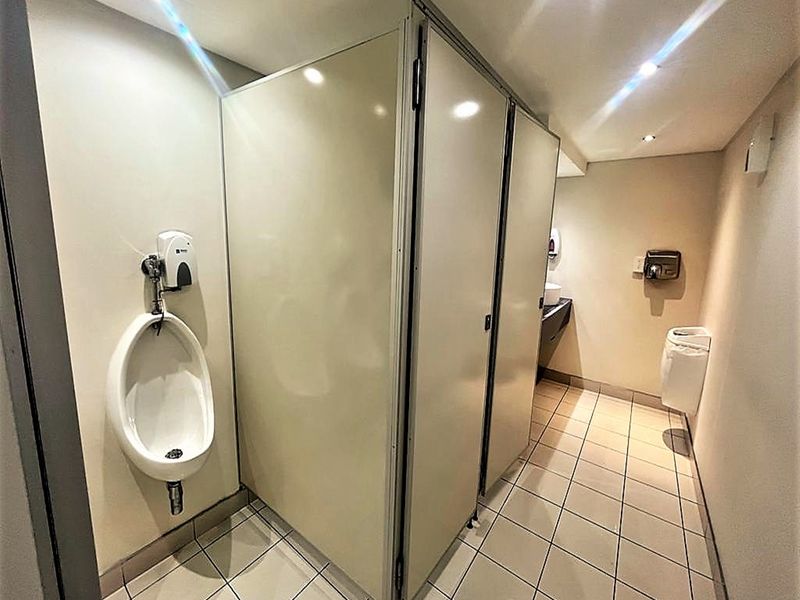 A functional office restroom featuring tiled flooring, multiple toilet cubicles, and wall-mounted sanitary fixtures including a urinal.