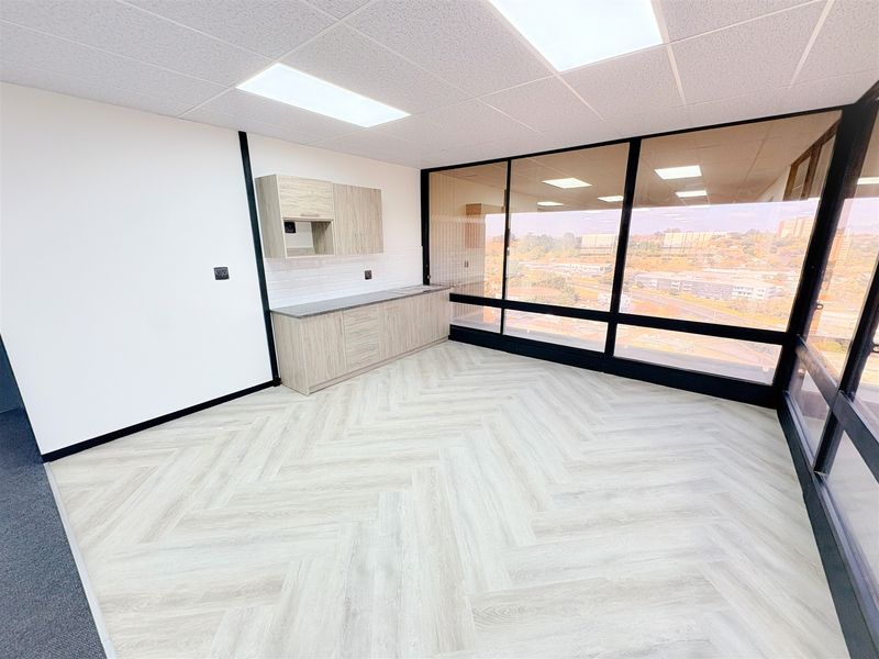 Modern office space featuring herringbone vinyl flooring, built-in kitchenette cabinetry, and expansive windows providing ample natural light and elevated views.