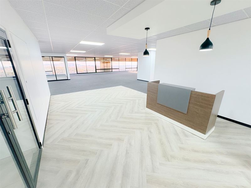 Modern office reception area featuring herringbone flooring, a built-in reception desk, pendant lighting, and expansive floor-to-ceiling windows with panoramic views.