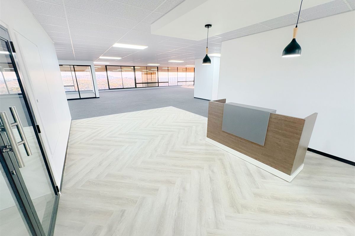 Modern office reception area featuring herringbone flooring, a built-in reception desk, pendant lighting, and expansive floor-to-ceiling windows with panoramic views.