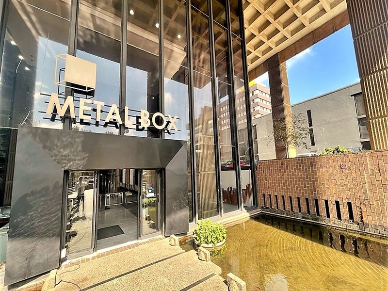 Modern office building entrance featuring a striking glass facade, architectural concrete waffle ceiling, and a decorative water feature at the main entry point.