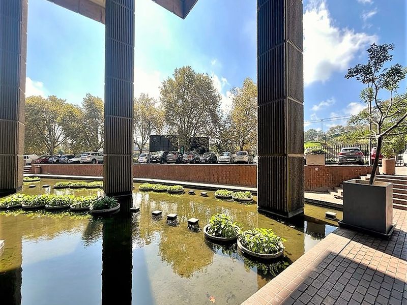 A well-maintained outdoor courtyard area featuring a decorative water feature, concrete structural columns, and brick paved walkways.
