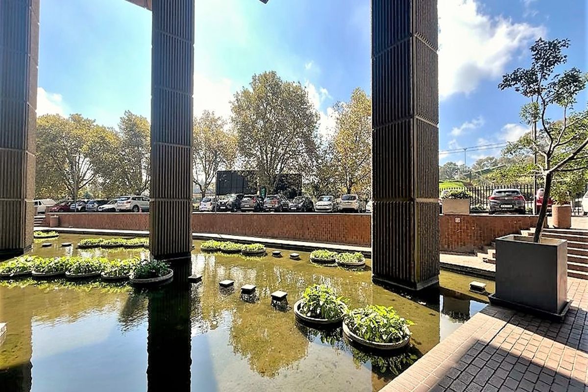 A well-maintained outdoor courtyard area featuring a decorative water feature, concrete structural columns, and brick paved walkways.