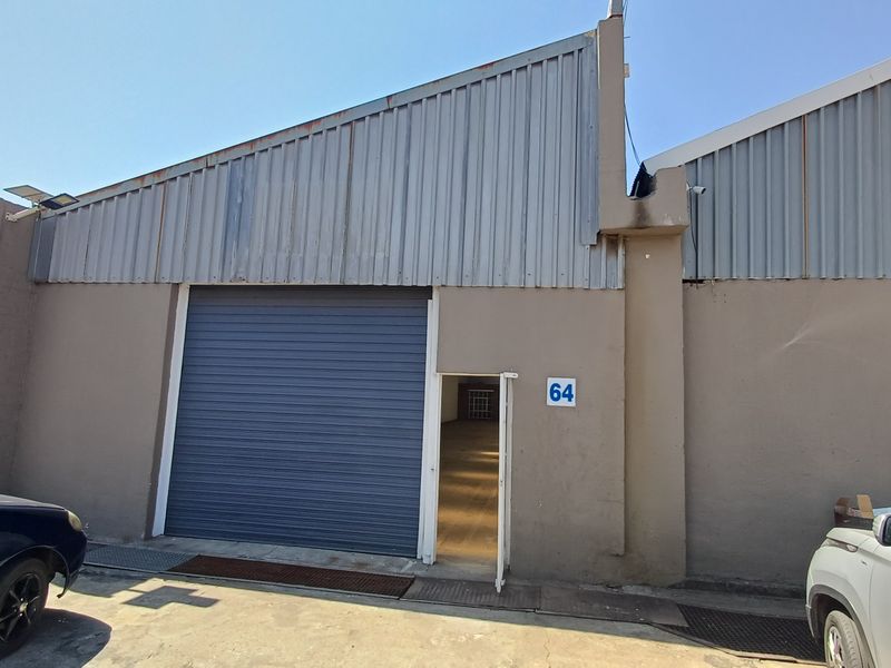 Industrial unit exterior featuring a roller shutter door, metal cladding, and a pedestrian entrance, suitable for warehouse or workshop operations.