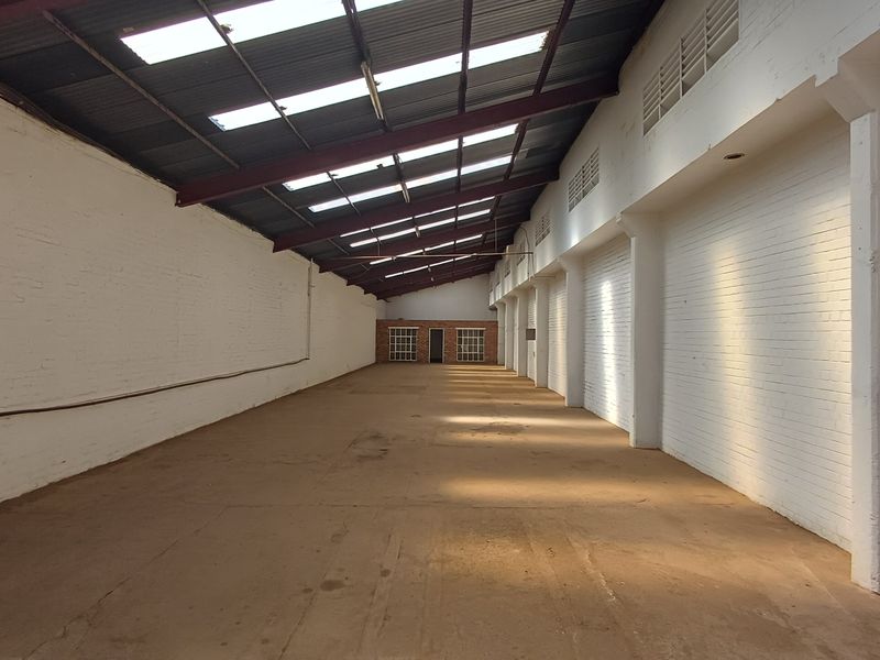 Spacious industrial warehouse unit featuring high ceilings with exposed steel trusses, natural light from skylights, painted brick walls, and durable concrete flooring.