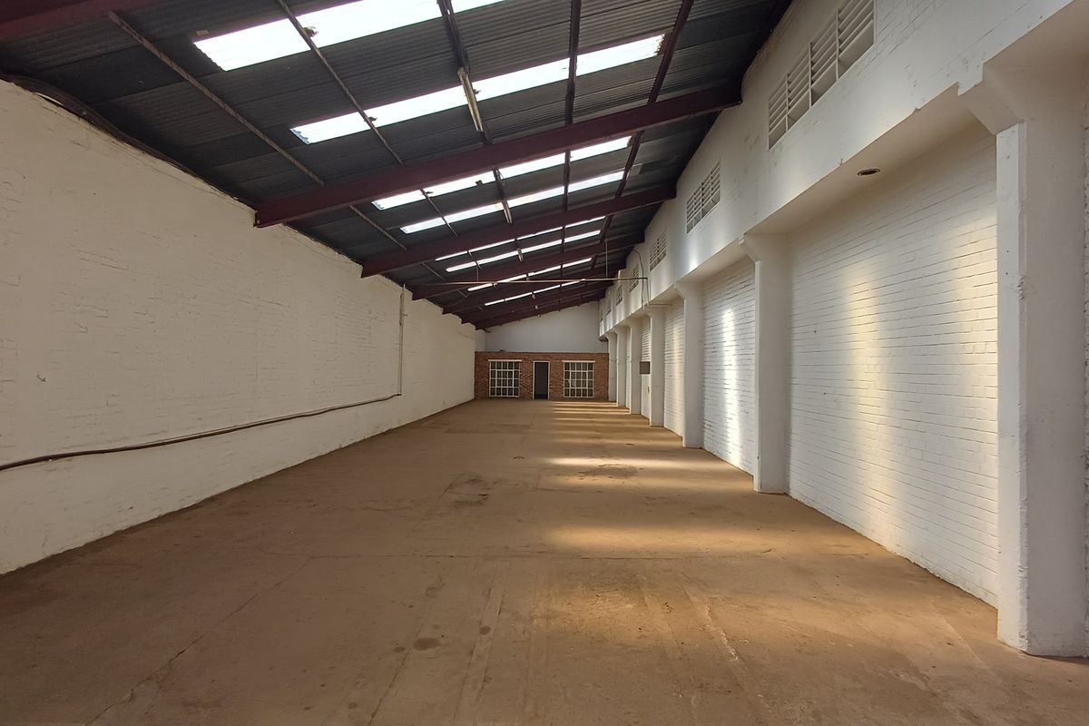 Spacious industrial warehouse unit featuring high ceilings with exposed steel trusses, natural light from skylights, painted brick walls, and durable concrete flooring.
