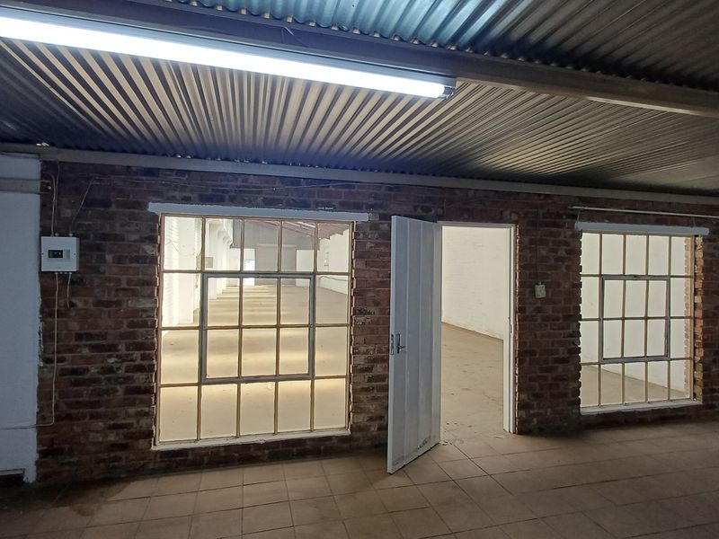 An industrial utility space featuring exposed brick walls, corrugated metal ceiling, tiled flooring, and steel-framed windows, offering a versatile open-plan layout.