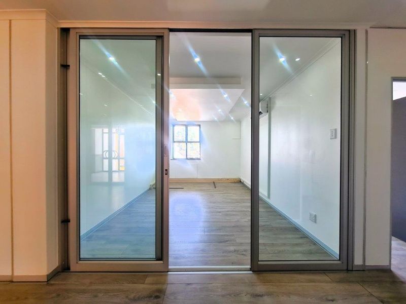 A bright, empty office space featuring modern sliding glass doors, recessed lighting, and wood-look laminate flooring.