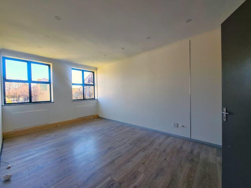 A bright, empty office space featuring modern laminate flooring, recessed downlighting, and large windows providing ample natural light.