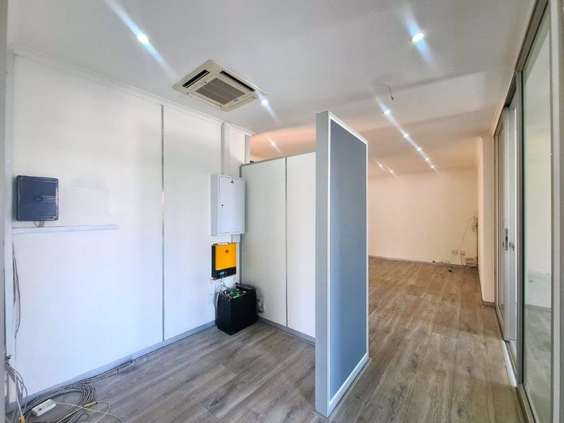 An open-plan office space featuring laminate flooring, recessed lighting, a cassette air conditioning unit, and a partition wall with integrated power infrastructure.