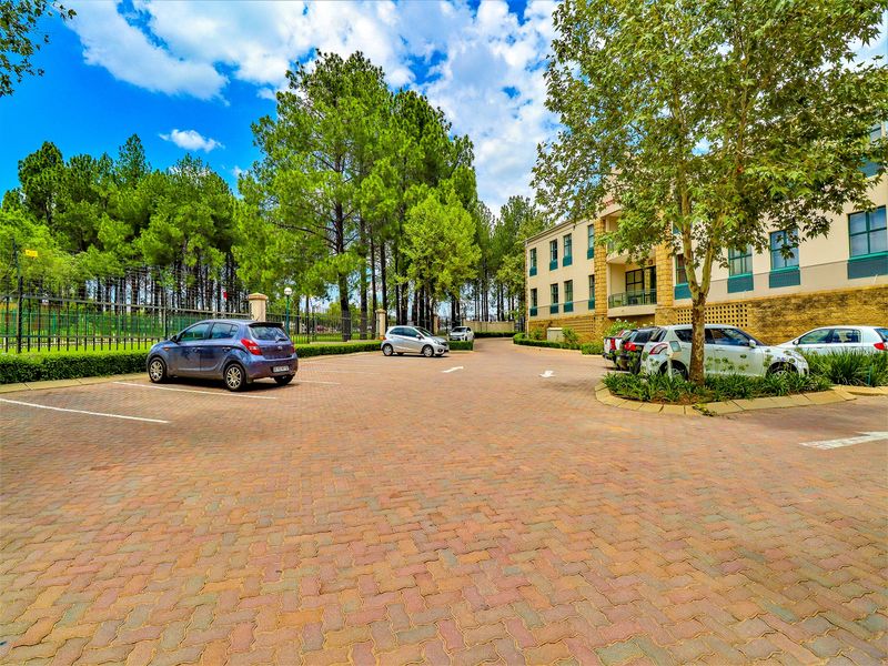 A well-maintained office building exterior featuring a paved parking lot, mature trees, and landscaped grounds.