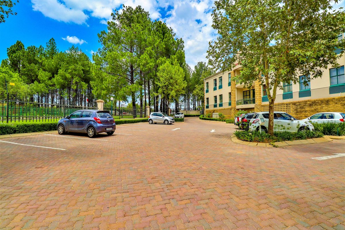 A well-maintained office building exterior featuring a paved parking lot, mature trees, and landscaped grounds.