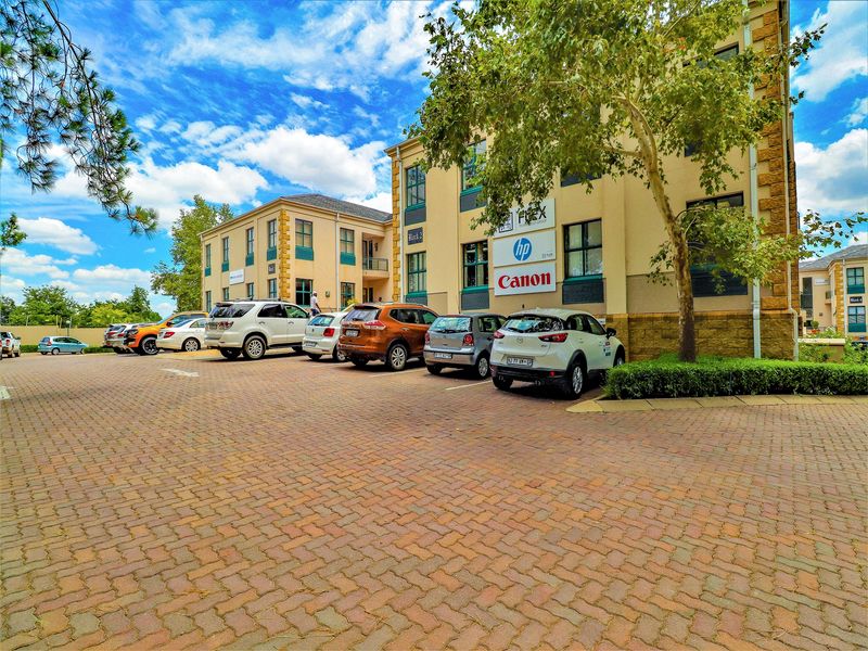 Exterior view of a multi-story office building featuring a paved parking area and established landscaping.