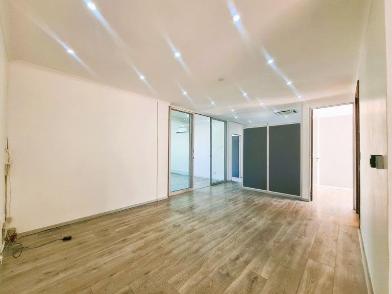 A bright, modern office space featuring laminate wood flooring, recessed downlighting, built-in storage, and sliding glass partitions for a flexible workspace layout.