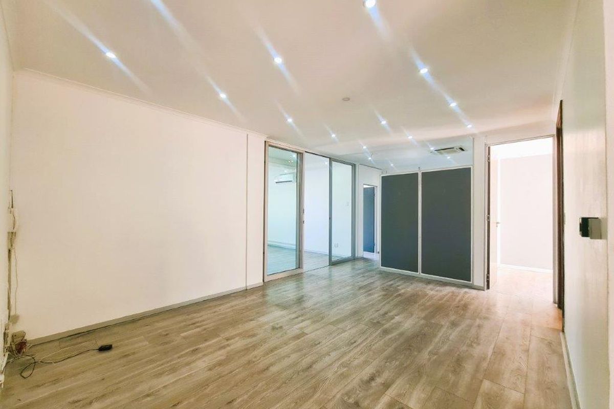A bright, modern office space featuring laminate wood flooring, recessed downlighting, built-in storage, and sliding glass partitions for a flexible workspace layout.