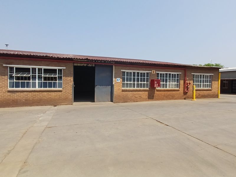 Industrial unit exterior featuring a brick facade, steel-framed windows, a large sliding entrance door, and a paved concrete yard area.