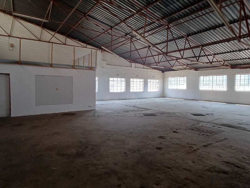 Spacious industrial utility area featuring high exposed steel roof trusses, concrete flooring, and a mezzanine level, suitable for warehouse or workshop use.