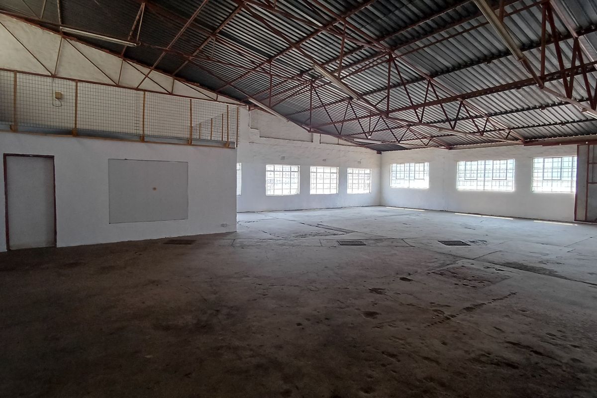 Spacious industrial utility area featuring high exposed steel roof trusses, concrete flooring, and a mezzanine level, suitable for warehouse or workshop use.