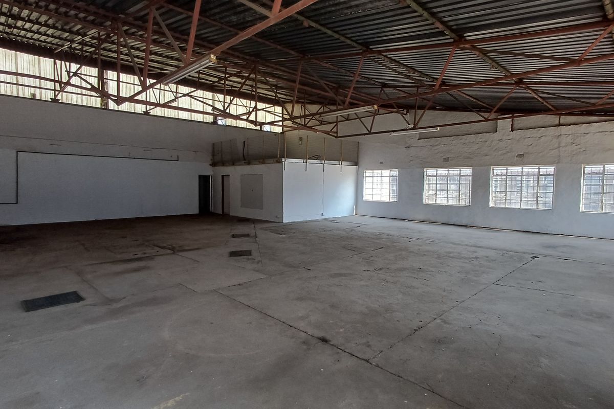 Spacious industrial utility area featuring high-volume exposed steel roof trusses, concrete flooring, and multiple security-barred windows providing ample natural light.