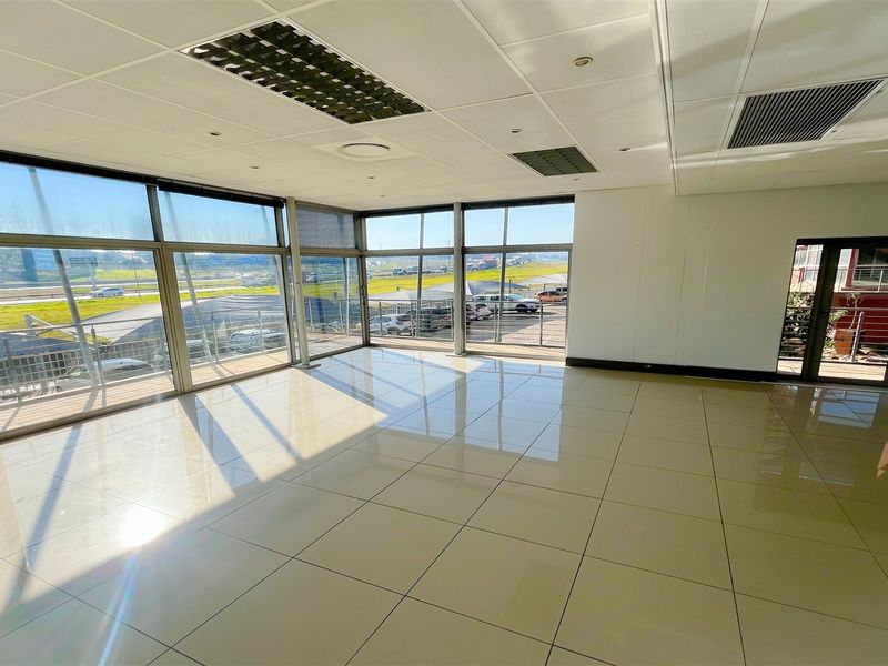A bright, open-plan office space featuring large floor-to-ceiling windows, polished ceramic tile flooring, and a modern suspended ceiling with integrated lighting.