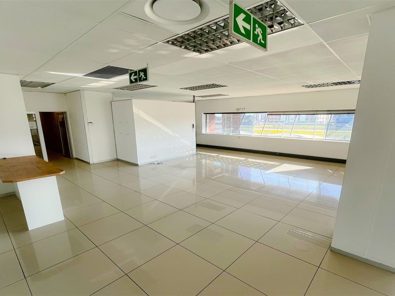A bright, open-plan office space featuring polished ceramic tile flooring, suspended ceilings with recessed lighting, and large windows providing ample natural light.