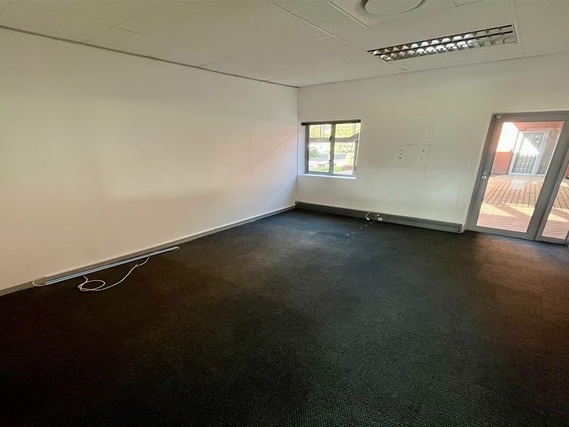 An empty office space featuring a suspended ceiling, recessed lighting, carpeted flooring, and direct access to an outdoor patio area.