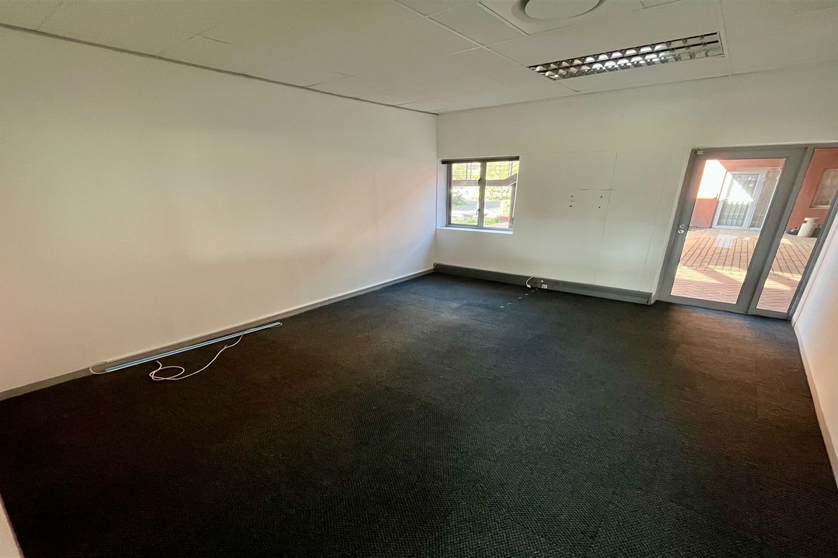 An empty office space featuring a suspended ceiling, recessed lighting, carpeted flooring, and direct access to an outdoor patio area.