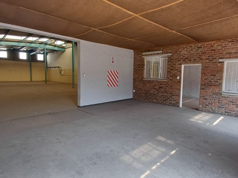 Spacious industrial open-plan area featuring exposed brick walls, concrete flooring, and high-clearance steel roof trusses, suitable for warehouse or workshop use.
