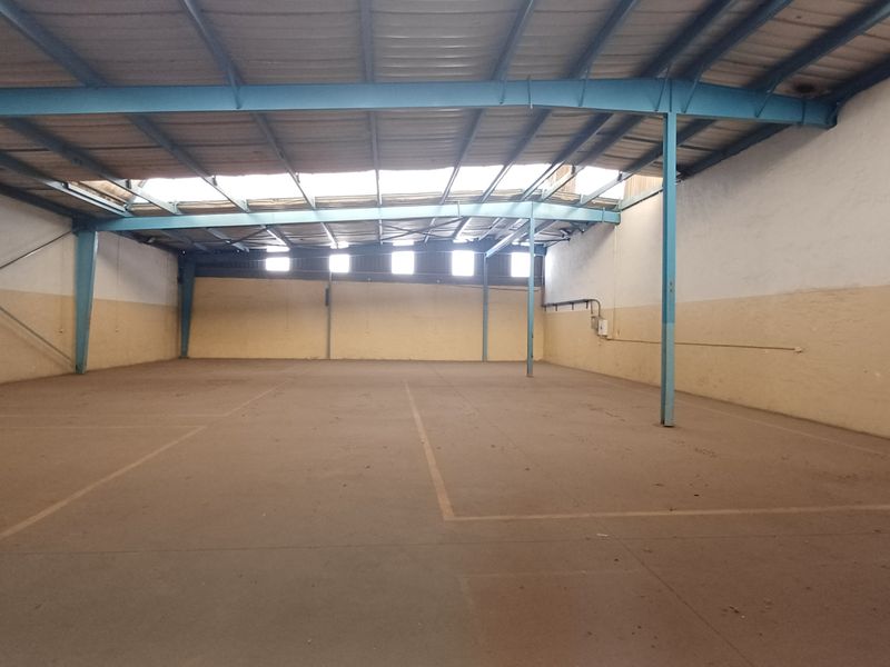 Spacious industrial warehouse unit featuring exposed steel roof trusses, concrete flooring, and natural light through skylight panels.