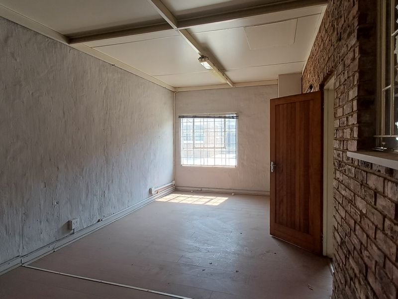An empty office space featuring exposed brickwork, a timber door, security-barred windows, and a suspended ceiling, offering a functional industrial workspace.