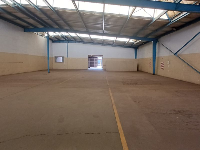 Spacious industrial warehouse unit featuring high ceilings with exposed steel trusses, concrete flooring, and natural light through integrated skylight panels.