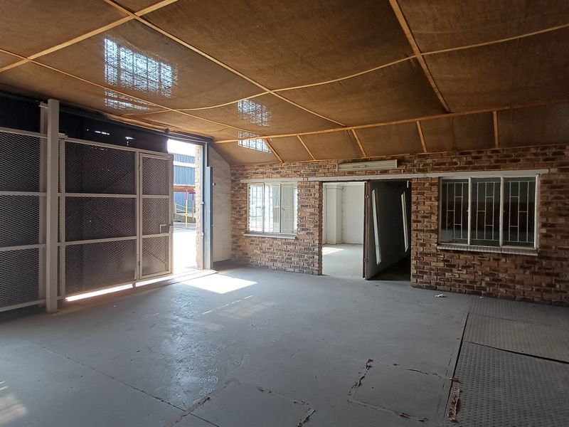 Spacious industrial utility area featuring exposed brick walls, concrete flooring, and a suspended mesh ceiling, suitable for workshop or storage use.