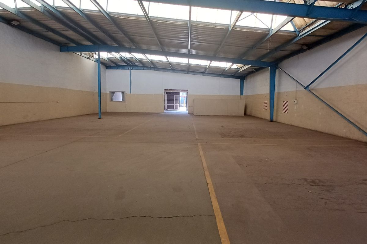 Spacious industrial warehouse unit featuring high ceilings with exposed steel trusses, concrete flooring, and natural light through integrated skylight panels.
